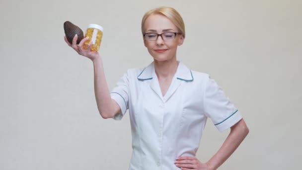 Nutritionist doctor holding organic avocado fruit and jar of medicine or vitamin or omega 3 capsules — Stock Video