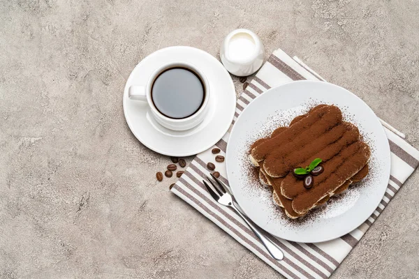 Classic tiramisu dessert on ceramic plate, milk or cream and cup of coffee on concrete background — Stock Photo, Image