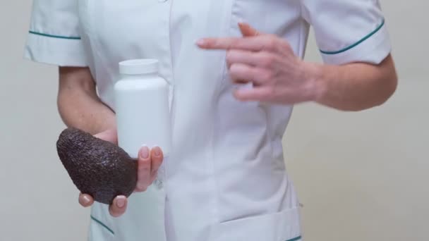 Dokter ahli gizi memegang buah alpukat organik dan sebotol obat atau vitamin atau omega 3 kapsul — Stok Video