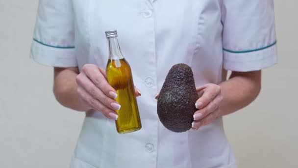Nutriční lékař drží organické avokádo ovoce a láhev oleje — Stock video