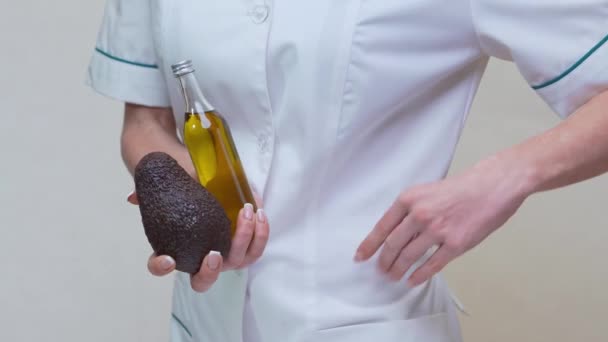 Beslenme uzmanı doktor elinde organik avokado meyvesi ve bir şişe yağ tutuyor. — Stok video