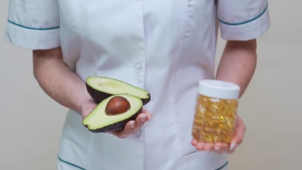 Nutritionist doctor holding organic avocado fruit and jar of medicine or vitamin or omega 3 capsules — Stock Video