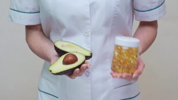 Nutritionist doctor holding organic avocado fruit and jar of medicine or vitamin or omega 3 capsules — Stock Video