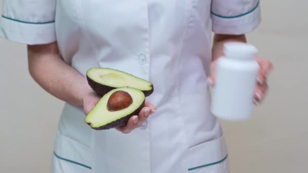 Nutricionista médico sosteniendo fruta de aguacate orgánica y frasco de medicamento o vitaminas o omega 3 cápsulas — Vídeos de Stock