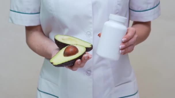 Врач-диетолог держит органические фрукты авокадо и банку лекарств или витамины или омега 3 капсулы — стоковое видео