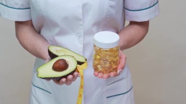 Voedingsdeskundige arts met biologische avocado fruit en een pot van de geneeskunde of vitamine of omega 3 capsules — Stockvideo