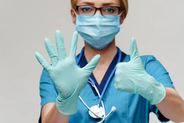 Arts verpleegkundige vrouw met stethoscoop dragen beschermende masker en rubber of latex handschoenen tonen op zichzelf — Stockfoto
