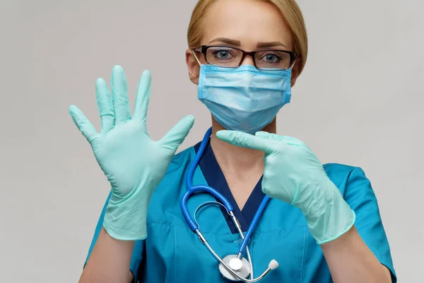 Médico enfermera mujer con estetoscopio con máscara protectora y guantes de goma o látex mostrando a sí misma —  Fotos de Stock