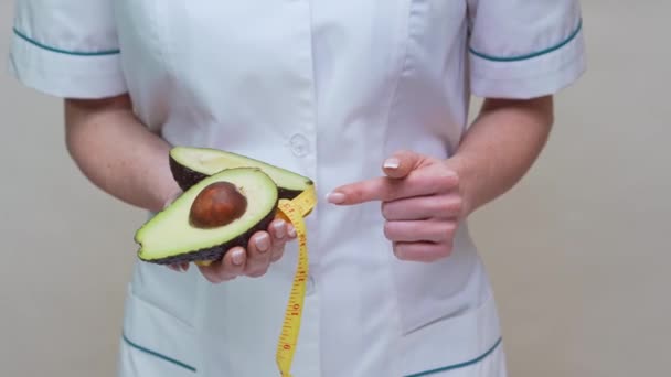 Nutritionist doctor healthy lifestyle concept - holding organic avocado fruit and measuring tape — Stock Video