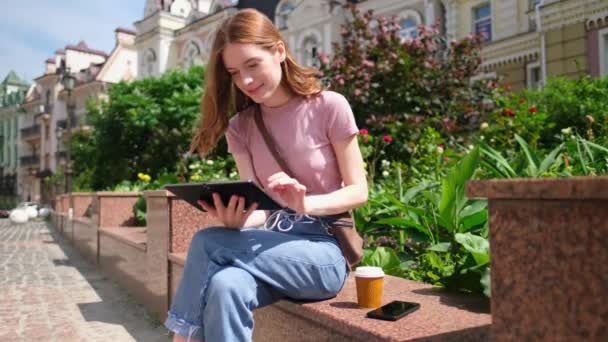 Hermosa mujer joven turista con café para llevar en el centro de la ciudad usando tableta pc — Vídeo de stock