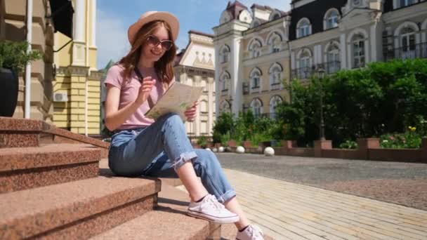 美丽的年轻女性游客，坐在市中心的楼梯上，带着城市地图，快乐极了 — 图库视频影像