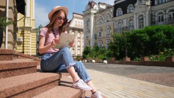 美丽的年轻女性游客，坐在市中心的楼梯上，带着城市地图，快乐极了 — 图库视频影像