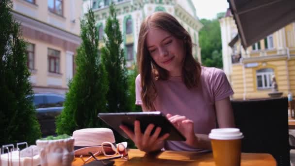 Молода жінка використовує планшетний ПК в кафе на літній терасі — стокове відео