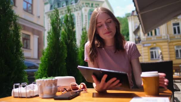 Молода жінка використовує планшетний ПК в кафе на літній терасі — стокове відео
