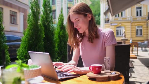 Yazlık terasta bir kafede dizüstü bilgisayar kullanan genç bir kadın. — Stok video