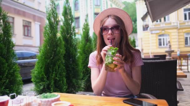 Молодая женщина разговаривает по телефону в кафе на летней террасе — стоковое видео