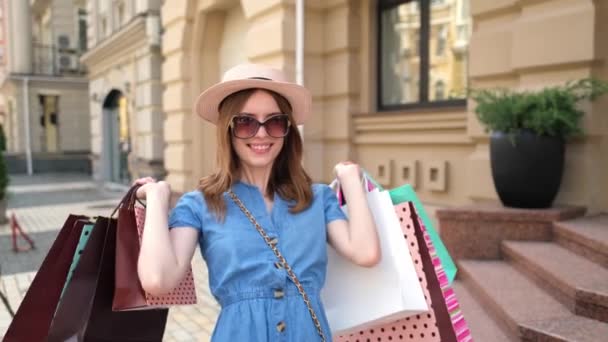 Молодая женщина с сумками для покупок гуляет по городу в летний день — стоковое видео