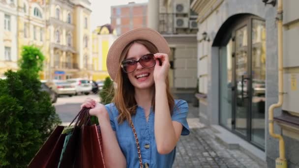 Mujer joven con bolsas de compras caminando en una ciudad en el día de verano — Vídeo de stock