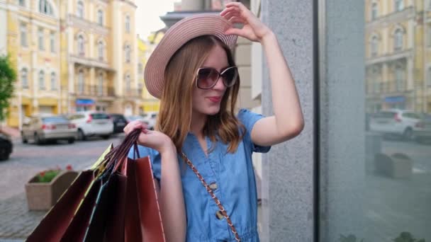 Молодая женщина с сумками для покупок гуляет по городу в летний день — стоковое видео