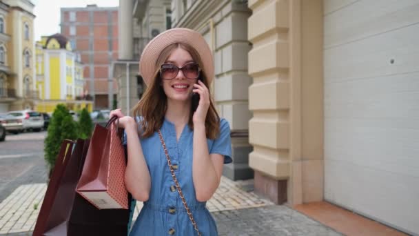 Mujer joven con bolsas de compras caminando en una ciudad en el día de verano — Vídeos de Stock