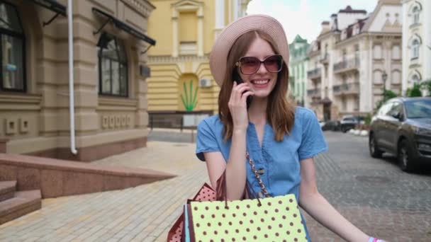 Mujer joven con bolsas de compras caminando en una ciudad en el día de verano — Vídeos de Stock