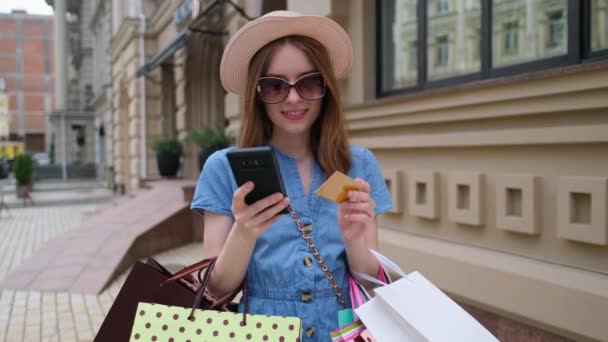 Mujer joven con bolsas de compras caminando en una ciudad en el día de verano — Vídeo de stock