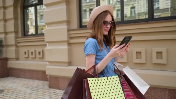 Mujer joven con bolsas de compras caminando en una ciudad en el día de verano — Vídeos de Stock