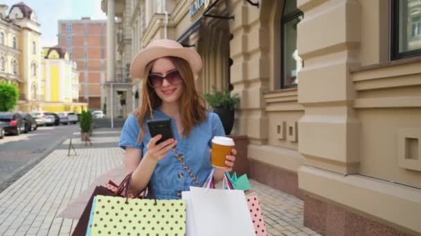 Mujer joven con bolsas de compras caminando en una ciudad en el día de verano — Vídeos de Stock