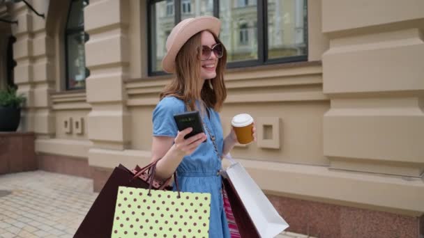 Mujer joven con bolsas de compras caminando en una ciudad en el día de verano — Vídeos de Stock