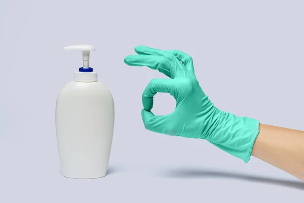 Mano femminile in guanto di gomma di lattice e disinfettante per le mani o dispenser di sapone liquido su fondo grigio chiaro — Foto Stock