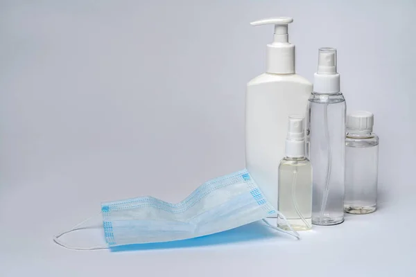 薄い灰色の背景に化粧水、消毒剤または液体石鹸と保護マスクのボトル — ストック写真