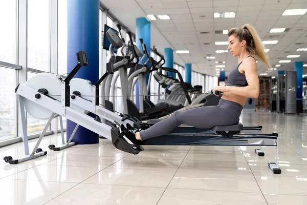 Young woman working out on row machine at gym exercising — Stock Photo, Image