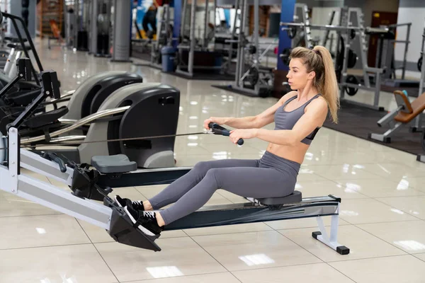 Junge Frau trainiert auf Rudergerät im Fitnessstudio — Stockfoto