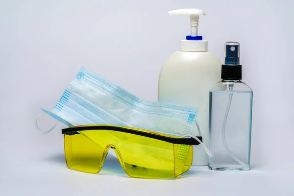 Flesje lotion, ontsmettingsmiddel of vloeibare zeep, bril en beschermmasker over lichtgrijze achtergrond — Stockfoto