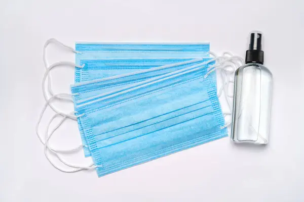 薄い灰色の背景に隔離された化粧水、消毒剤または液体石鹸と医療用保護マスクのボトル — ストック写真