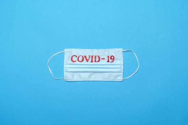 Mascarilla médica azul desechable con signo COVID-19 sobre fondo azul —  Fotos de Stock