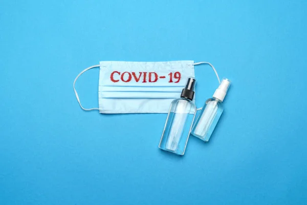 Mascarilla médica azul desechable con signo COVID-19 y antiséptico desinfectante de manos con alcohol sobre fondo azul —  Fotos de Stock