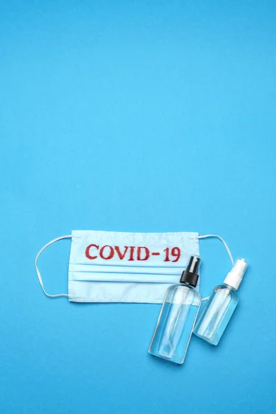 Mascarilla médica azul desechable con signo COVID-19 y antiséptico desinfectante de manos con alcohol sobre fondo azul —  Fotos de Stock