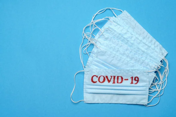Pila de mascarillas médicas azules desechables con signo COVID-19 sobre fondo azul —  Fotos de Stock