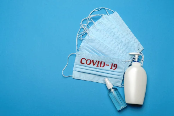 Pila de mascarillas médicas azules desechables con signo COVID-19 y desinfectante de manos con alcohol antiséptico sobre fondo azul —  Fotos de Stock