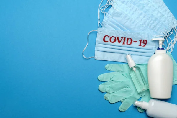 Pila de mascarillas médicas azules desechables con signo COVID-19, guantes de látex de goma y desinfectante de manos con alcohol antiséptico sobre fondo azul —  Fotos de Stock