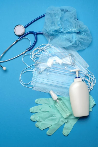 Egy halom eldobható kék orvosi arc maszkok, gumi latex kesztyű, szemüveg, sztetoszkóp és alkohol kézfertőtlenítő fertőtlenítő kék alapon — Stock Fotó