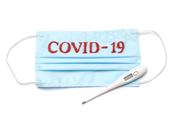 Mascarilla médica azul desechable con signo COVID-19 y termómetro electrónico aislado sobre fondo blanco con camino de recorte —  Fotos de Stock