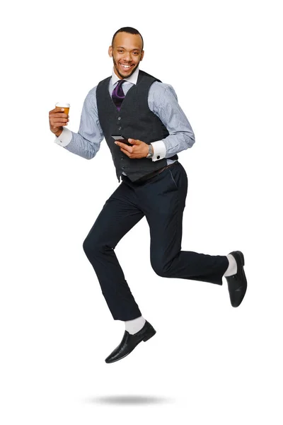 Щасливий молодий африканський бізнесмен стрибає високо і тримає каву, щоб піти і телефон ізольований на білому тлі — стокове фото
