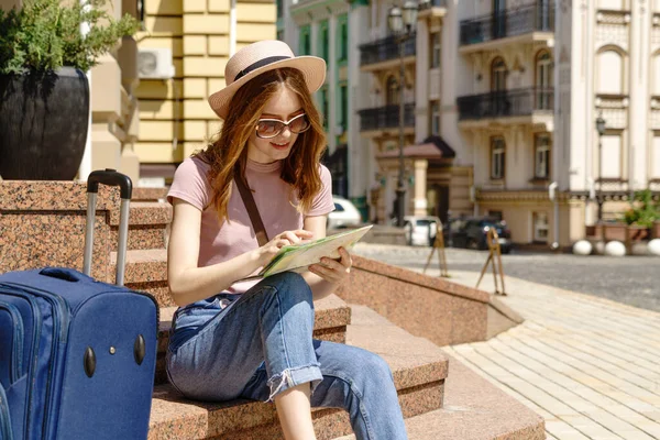 Bella Giovane Donna turista Piacevole con mappa della città e valigia seduta sulle scale — Foto Stock
