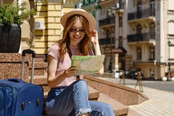 Bella Giovane Donna turista Piacevole con mappa della città e valigia seduta sulle scale — Foto Stock