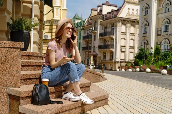 Красива молода жінка турист з кавою, що сидить на сходах за допомогою смартфона — стокове фото