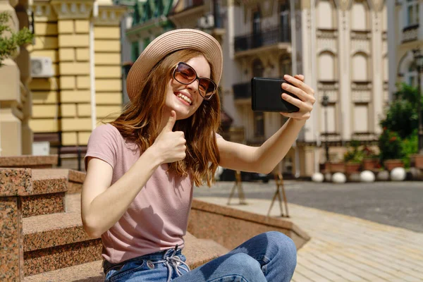 Hermosa mujer joven turista sentado en las escaleras usando smartphone haciendo videollamada o selfie —  Fotos de Stock