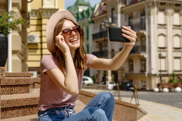 Hermosa mujer joven turista sentado en las escaleras usando smartphone haciendo videollamada o selfie — Foto de Stock