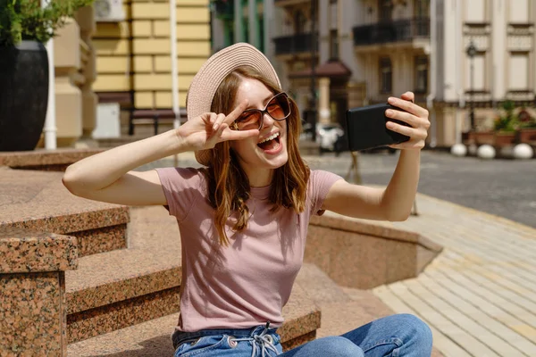 Piękna młoda kobieta turysta siedzi na schodach za pomocą smartfona podejmowania rozmowy wideo lub selfie — Zdjęcie stockowe